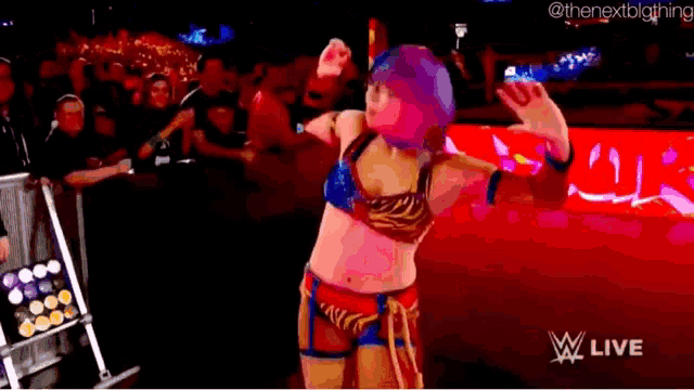 a female wrestler is dancing in front of a crowd while wearing a blue and red outfit .