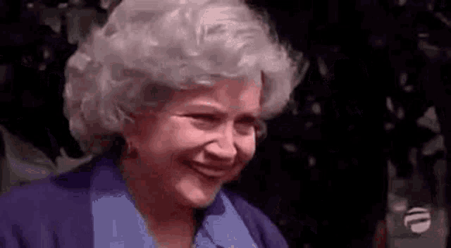 an elderly woman with gray hair is smiling while wearing a blue shirt .