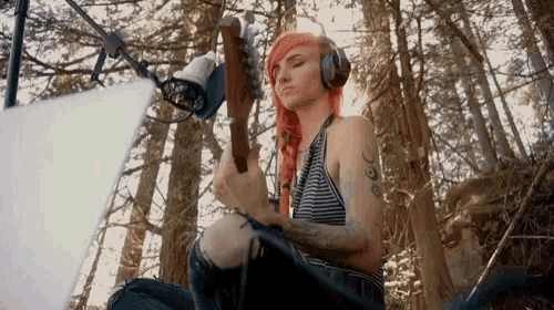 a woman wearing headphones is playing a guitar in a forest