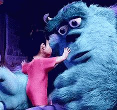 a little girl in a pink shirt is hugging a blue monster from monsters inc