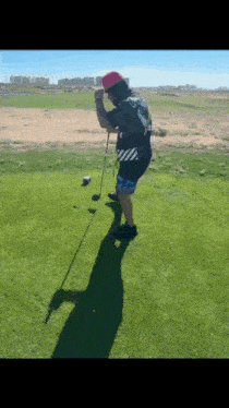 a man wearing a pink hat is swinging a golf club on a golf course