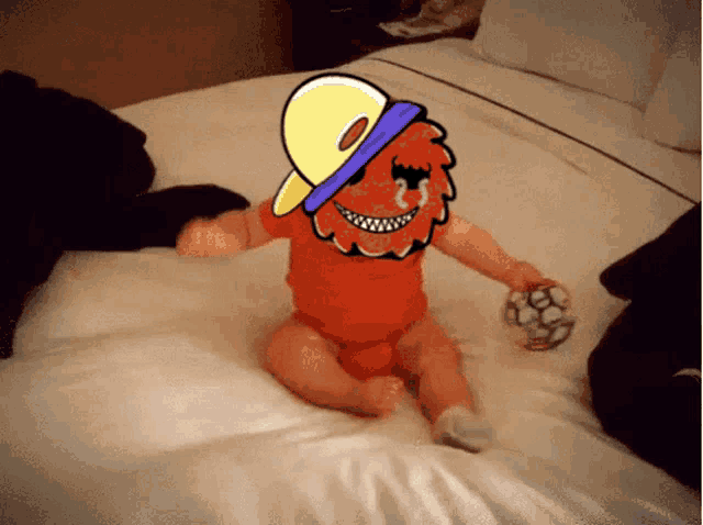 a baby wearing an orange bodysuit and a hat is laying on a bed