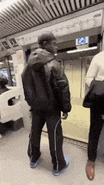 a man wearing a black jacket and crocs is standing in a train station .