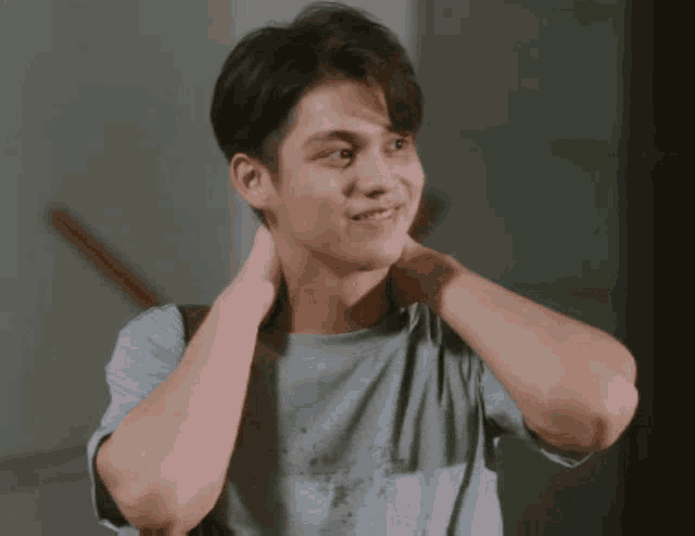 a young man in a blue shirt is holding his neck and smiling