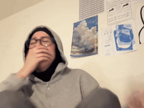 a person covering their mouth with their hand in front of a wall with posters on it