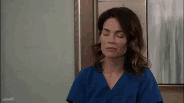 a woman in a blue scrub top with her eyes closed .