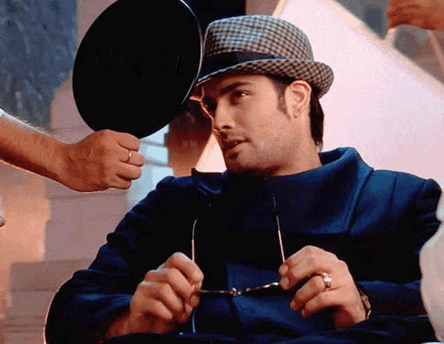 a man wearing a hat and glasses is looking at himself in the mirror