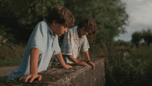 two young boys are looking over a wall