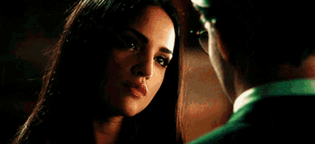 a man wearing glasses and a green suit looks at a woman