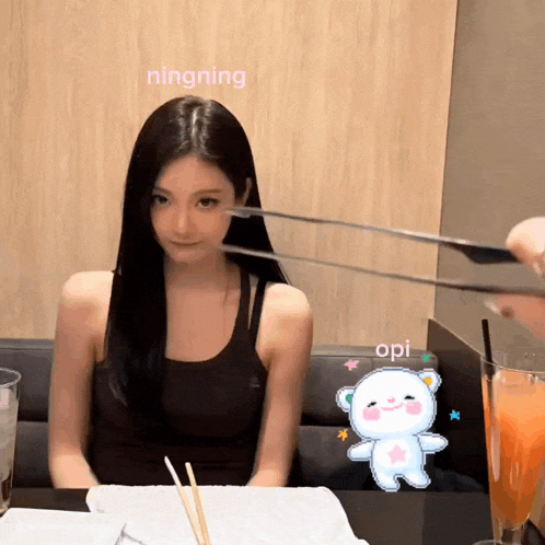 a woman sitting at a table with chopsticks and a sticker of a bear that says opi