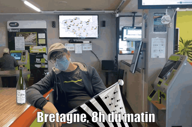 a man wearing a face mask is sitting at a table with a flag and the words bretagne 8h du matin written below him