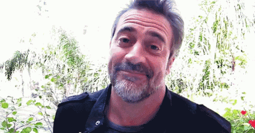 a man with a beard is making a funny face while standing in front of trees .