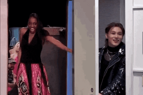 a woman in a pink dress and a man in a black jacket are standing next to each other in a doorway .