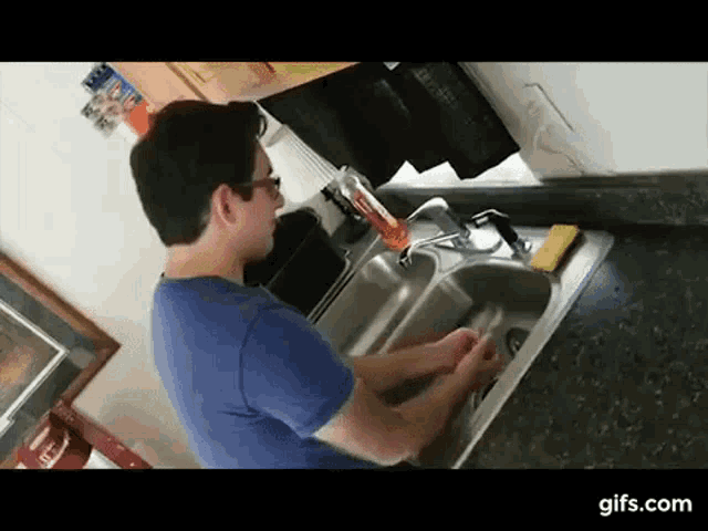 a man is washing his hands in a kitchen sink with a yellow sponge .