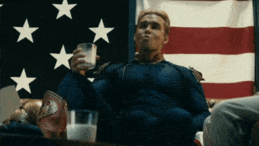 a man in a superhero costume sits in front of an american flag holding a glass of milk