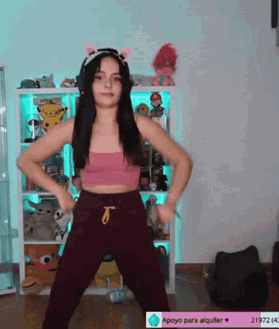 a girl in a pink top and purple pants is dancing in front of a shelf with stuffed animals