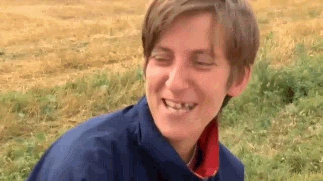 a young man with a missing tooth is smiling in a field of grass .