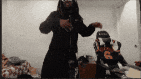 a man with dreadlocks is dancing in a room with a jersey with the number 6 on it