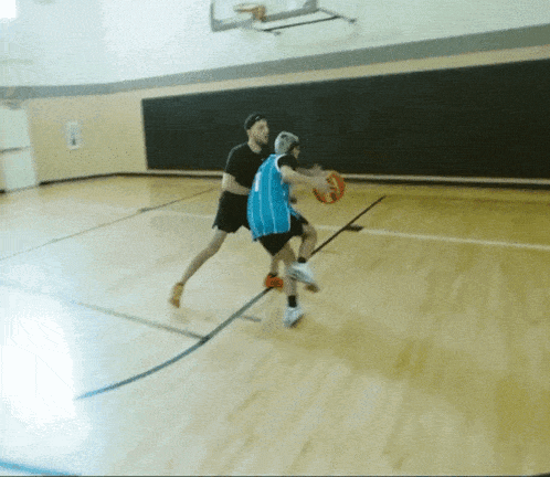 a man dribbles a basketball while another man tries to block it