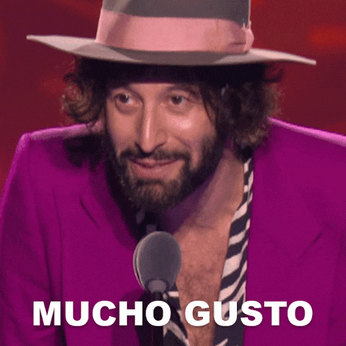 a man with a beard wearing a purple jacket and a hat says mucho gusto