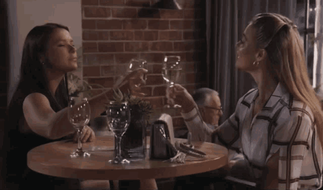 two women are sitting at a table with wine glasses