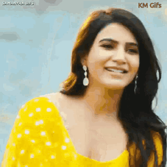 a woman wearing a yellow top and earrings is smiling