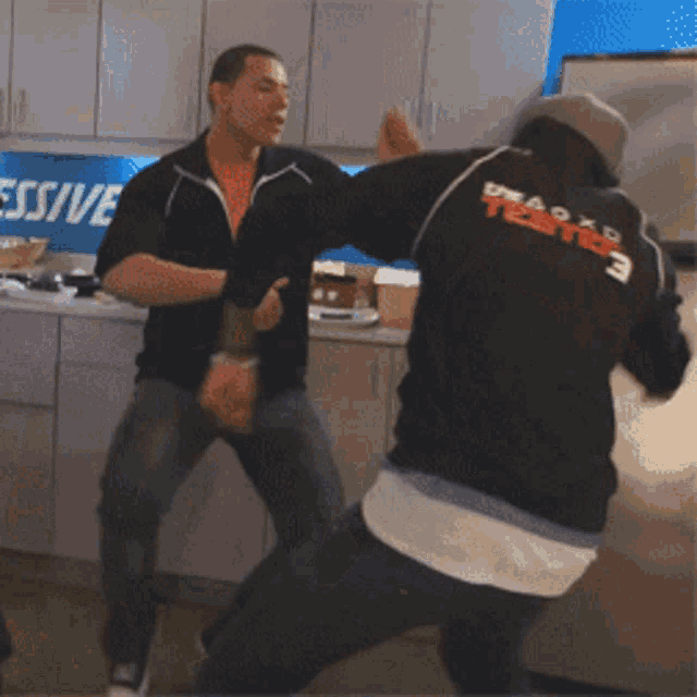 two men are fighting in a kitchen with a sign that says aggressive