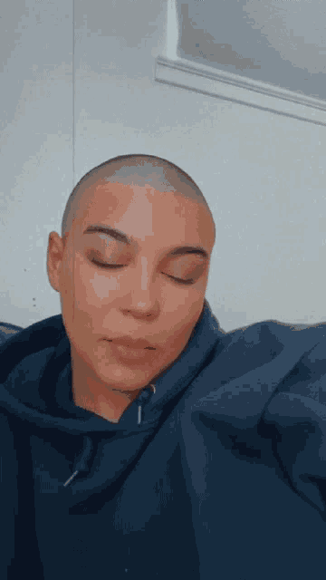 a woman with a shaved head is wearing a blue sweatshirt