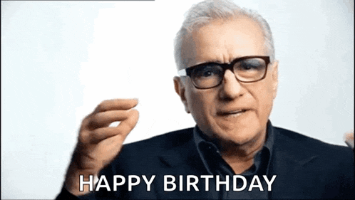 a man wearing glasses and a suit is giving a happy birthday sign .