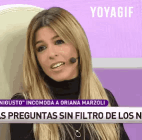 a woman with long blonde hair is sitting in front of a microphone on a purple background .