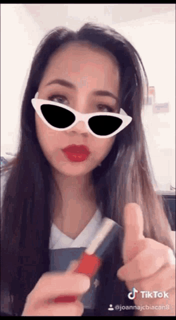 a woman wearing sunglasses and red lipstick giving a thumbs up sign