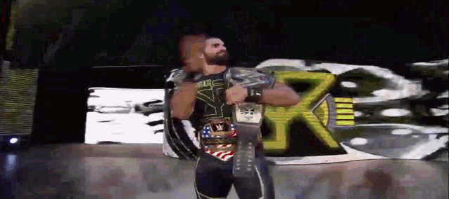 a wrestler is holding a wrestling championship belt in front of a large screen .