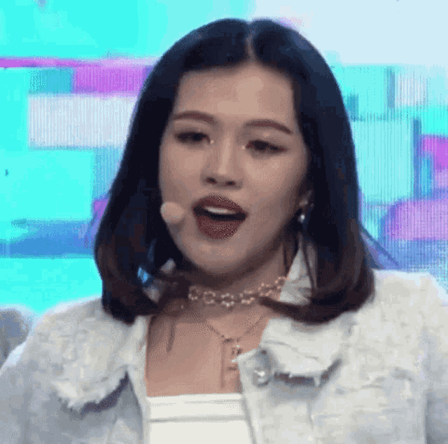 a woman wearing a choker and a white jacket is singing into a microphone on a stage .