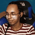 a woman wearing glasses and a striped shirt is sitting in a chair with a bandage on her face .
