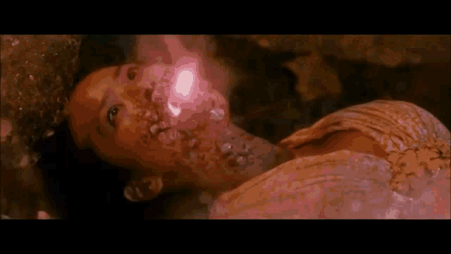 a woman is laying on the ground with a pink light shining on her face .