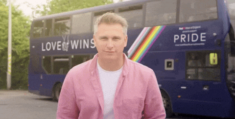 a man stands in front of a blue double decker bus that says pride