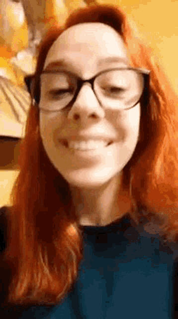 a woman with red hair and glasses is smiling at the camera .