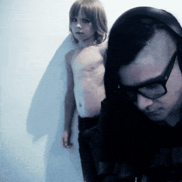a man wearing glasses stands next to a shirtless boy