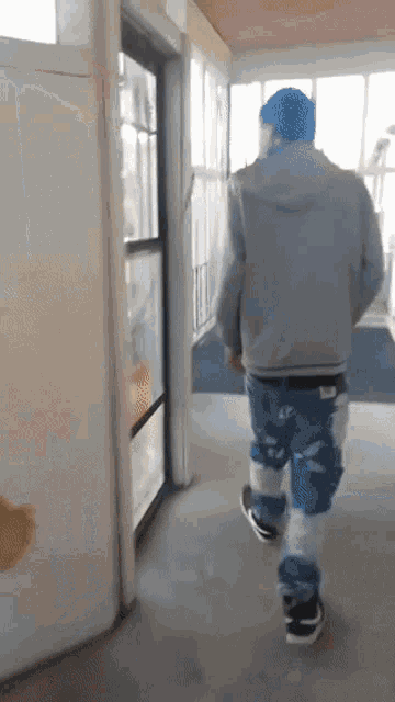a man wearing a blue hat and blue and white pants walks down a hallway