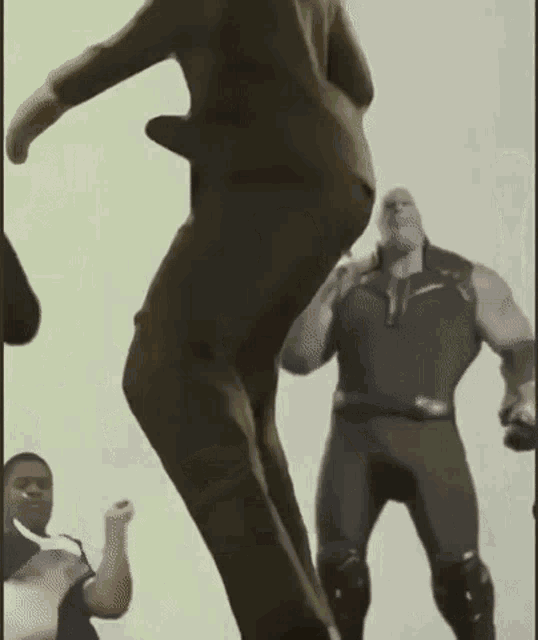 a man in a suit is jumping in the air while a man in a superhero costume stands behind him .