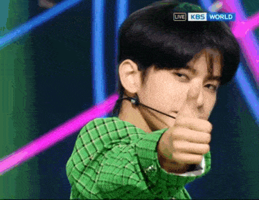 a man in a green plaid shirt is giving a thumbs up in front of a live kbs world sign