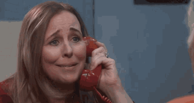 a woman is crying while holding a red telephone in her hands .