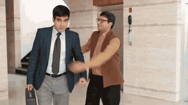 a man in a suit and tie is helping another man with his briefcase