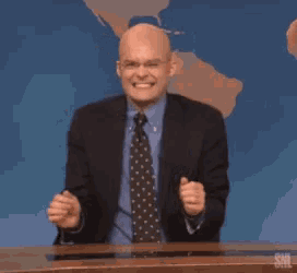 a man in a suit and tie is sitting at a desk with his hands in the air