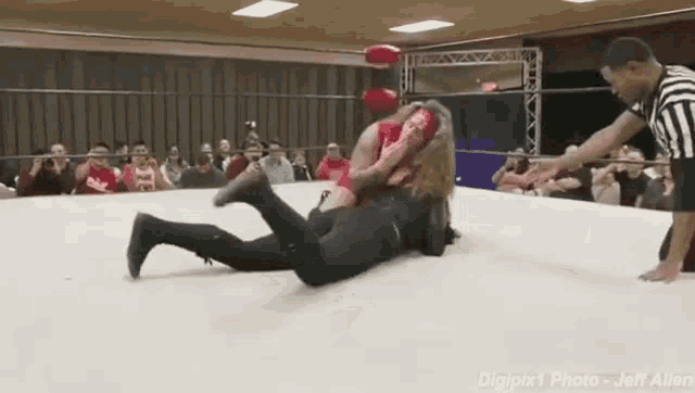 a woman is wrestling a man in a wrestling ring while a referee watches .