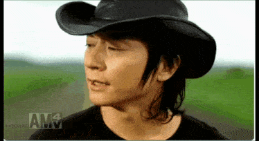 a man wearing a cowboy hat and a black shirt with am written on the bottom