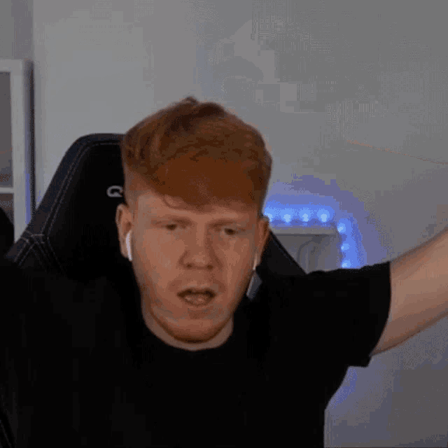 a man with red hair is sitting in a chair with his arms outstretched and wearing ear buds .