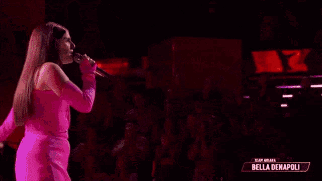 a woman wearing pink gloves is singing into a microphone on a stage .
