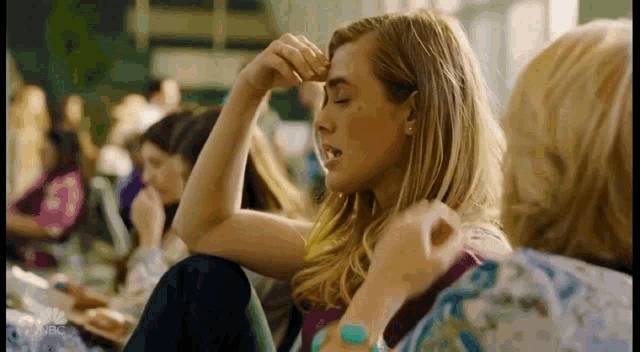 a woman is rubbing her forehead with her hand while sitting in a crowd of people .