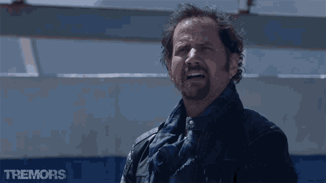 a man with a scarf around his neck is crying in front of a sign that says tremors